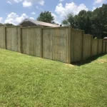 A wooden fence constructed from vertical planks, showcasing a natural wood finish, sturdy design, and surrounding yard filled with green grass.